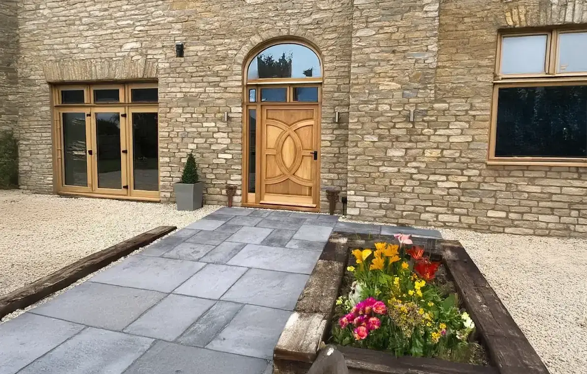 Bluestone walkway and landing leading to an arched front door with flower beds
