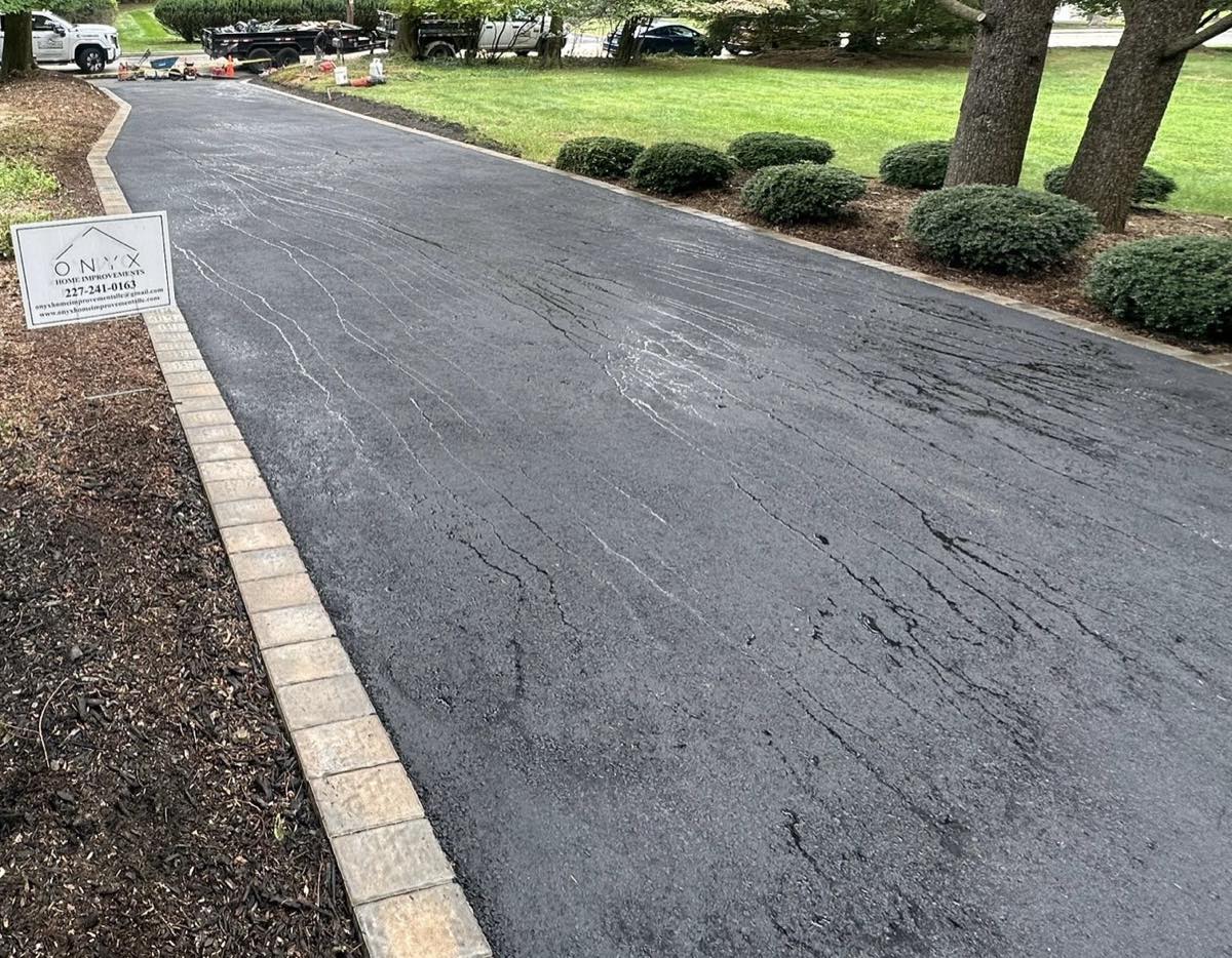 Freshly laid asphalt driveway edged with a tan paver border, running past clipped shrubs at a McLean home
