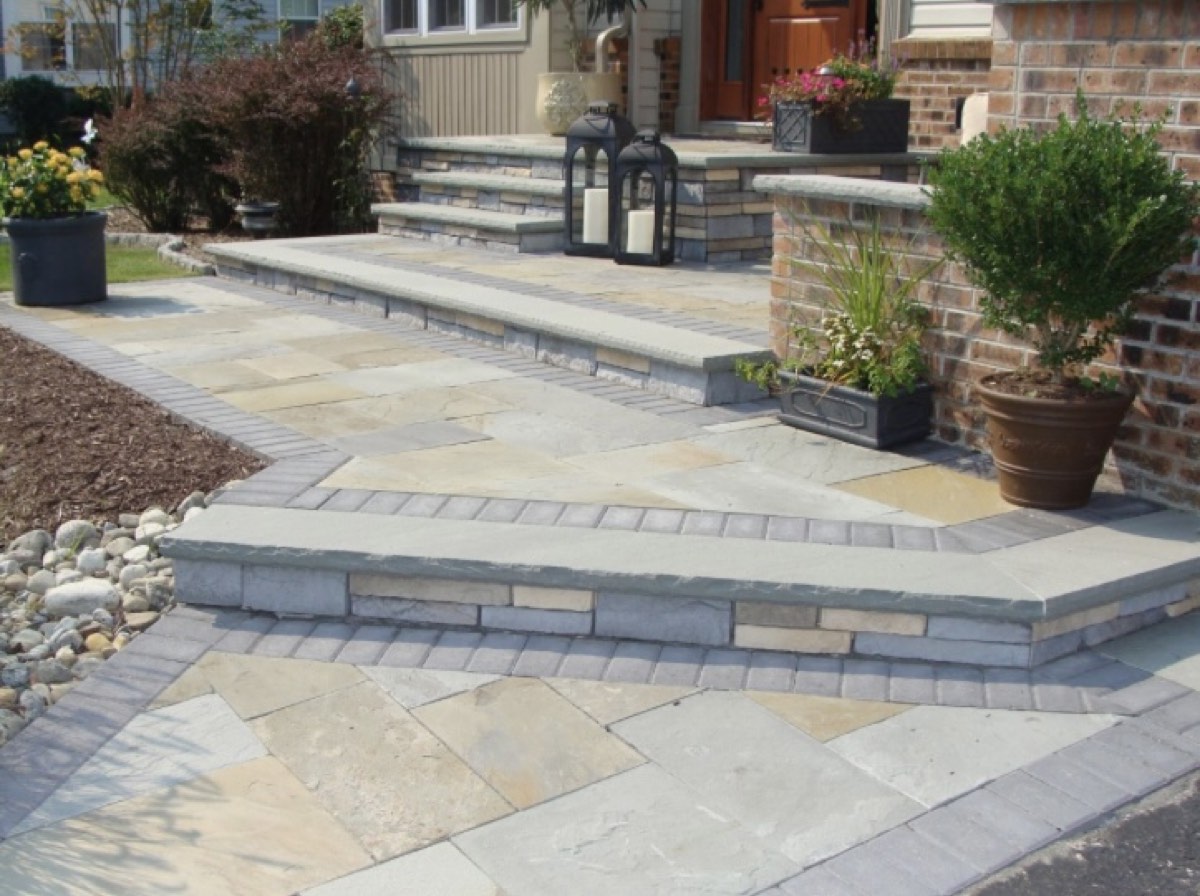 Irregular bluestone landing and steps with stone riser walls rising to the front door of a brick house, with lanterns and planters on the treads
