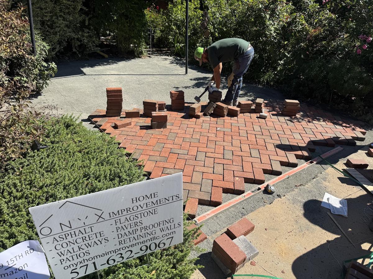 Onyx mason setting red clay brick pavers in a herringbone pattern with a mallet during installation in Arlington