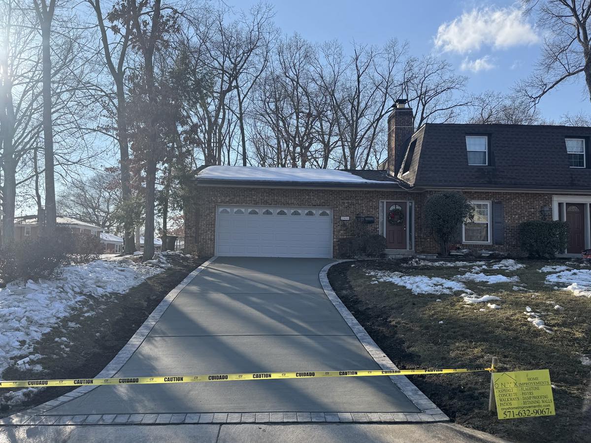 Broom-finished concrete driveway edged with a grey paver soldier course, curving to the garage of a brick Springfield home in winter