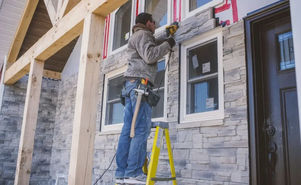 A builder installing natural stone veneer on the façade of a house.