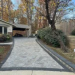 A stone veneer driveway and retaining wall sloped upwards towards a residential home.