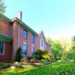 Close up of a stone retaining wall surrounded by green grass and a two story brick house.