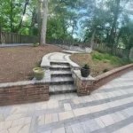 Long brick retaining wall in a backyard filled with dirt.