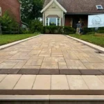 Long stone walkway leading up to a residential home. A sign on the front yard's grass says "Onyx Home Improvement LLC."