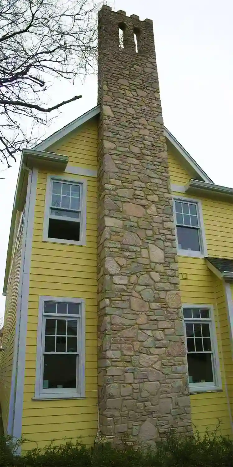 Tall chimney on the side of a two story house with yellow painted siding.