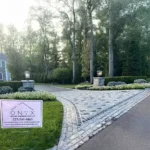 Front view of a stone driveway surrounded by tall trees and green grass.