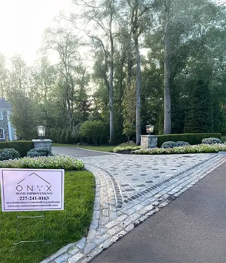 Front view of a stone driveway surrounded by tall trees and green grass.