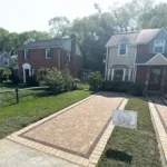 Front view of a stone driveway surrounded by two story homes and small front yards with patches of grass.