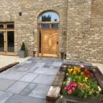 Professionally laid stone walkway and small garden in front of a big home with stone sidewalls.