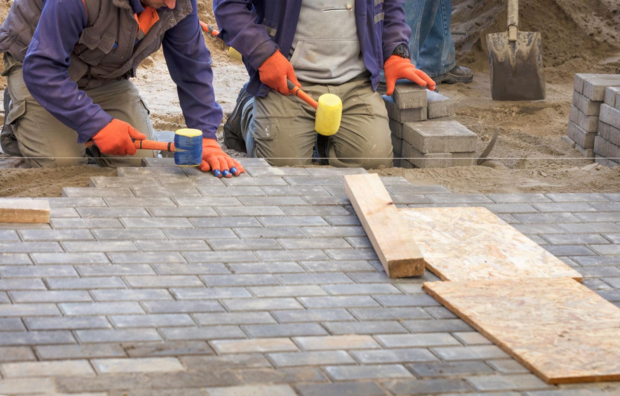 Workers lay and align driveway tiles using a guiding thread.