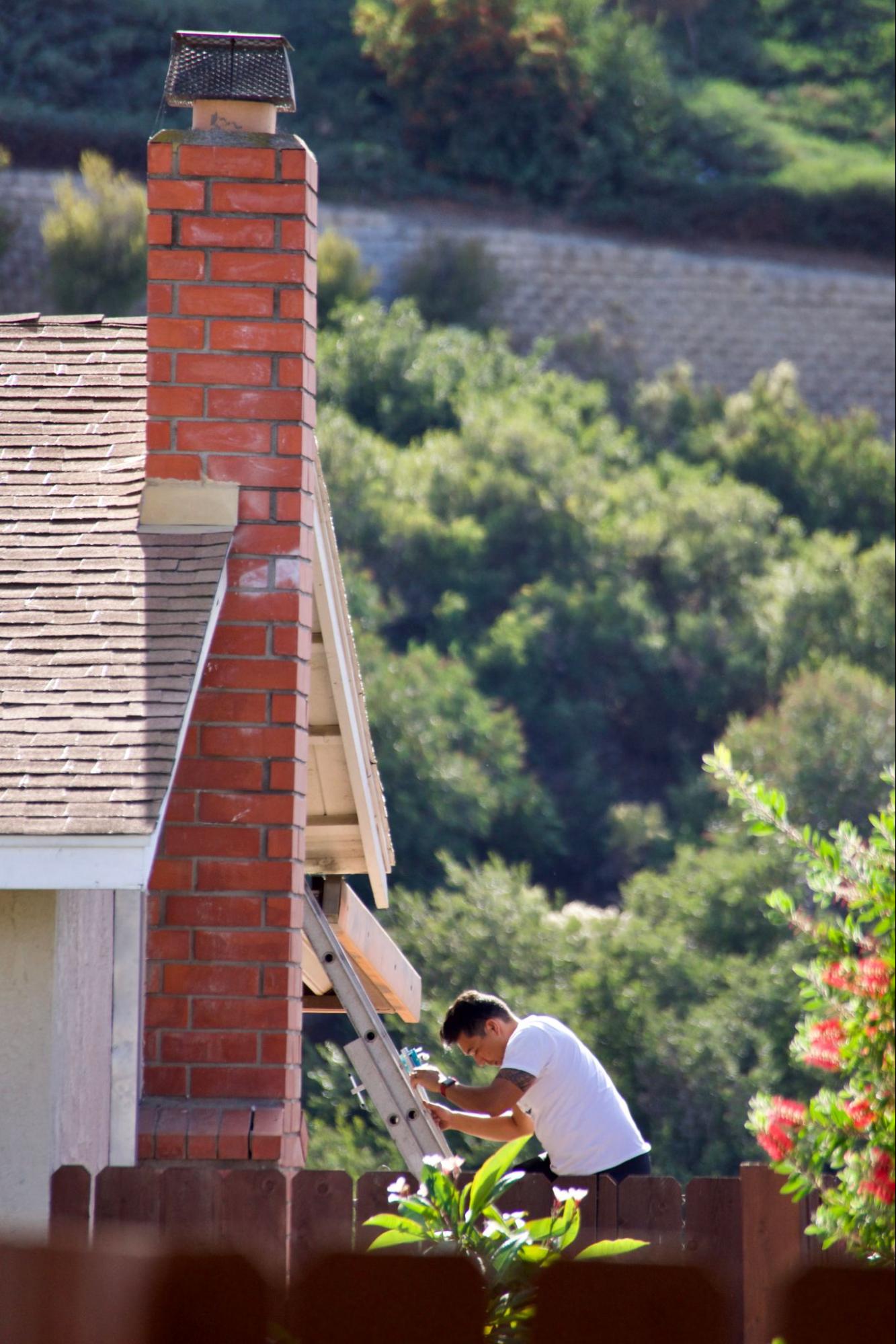 A man climbs down a ladder after inspecting his chimney for repairs.