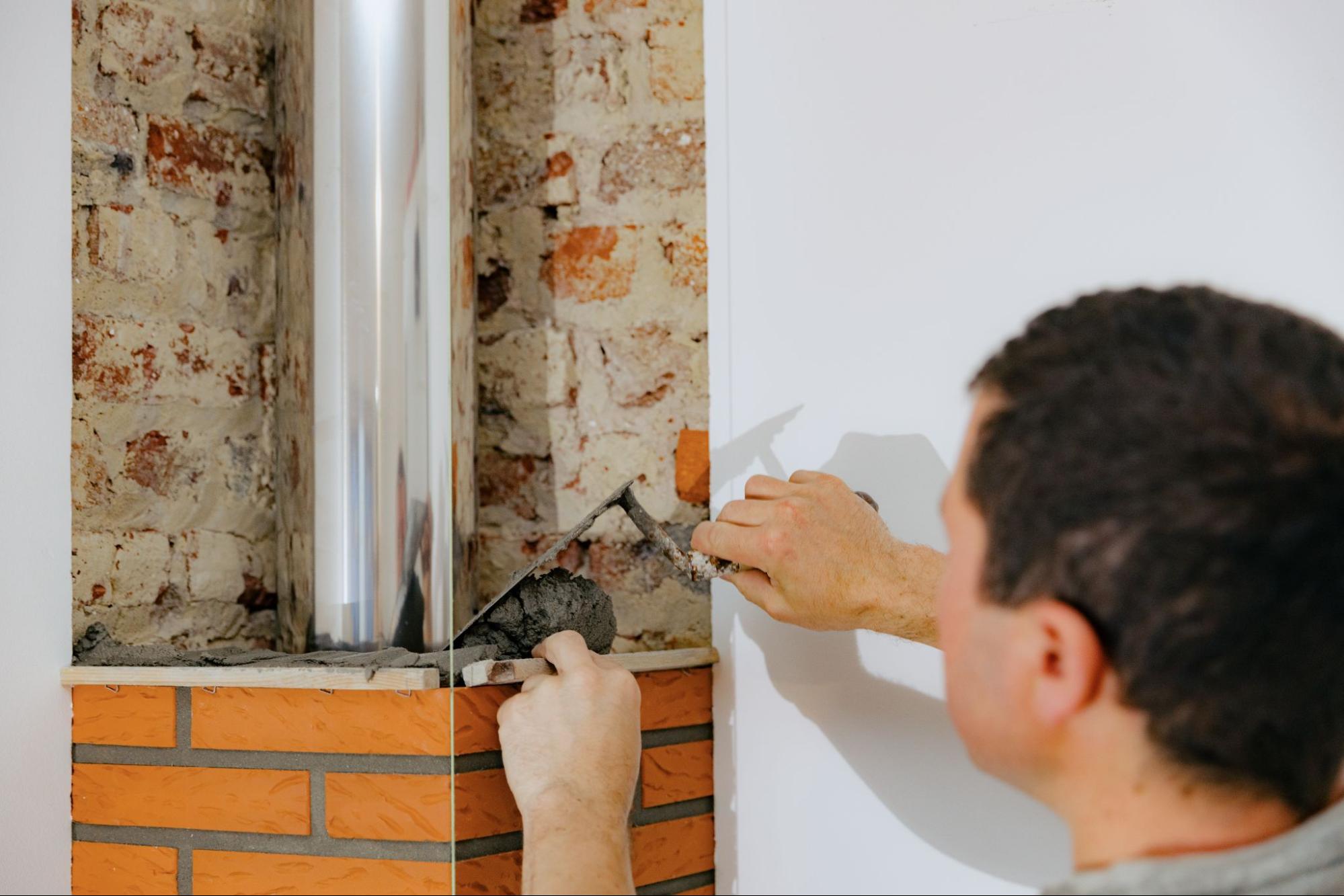A worker restores damaged brickwork on a chimney structure.