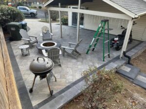 Backyard patio with fire pit, wood furniture, BBQ grill, and covered motorcycle parking.