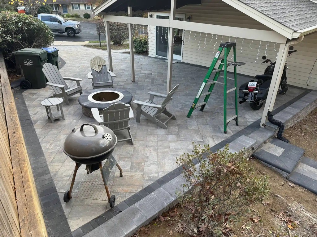 Backyard patio with fire pit, wood furniture, BBQ grill, and covered motorcycle parking.