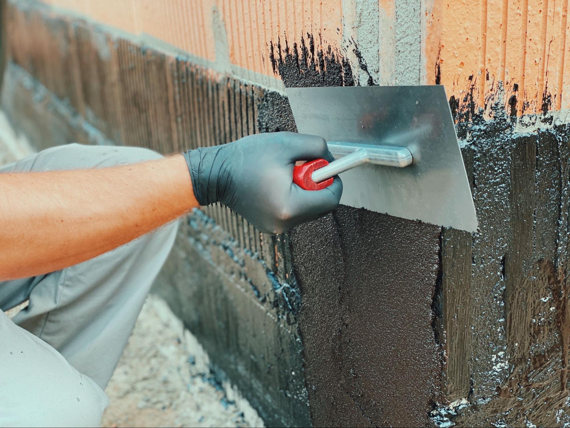 Worker applying protective coating to hollow bricks for foundation reinforcement and moisture resistance.