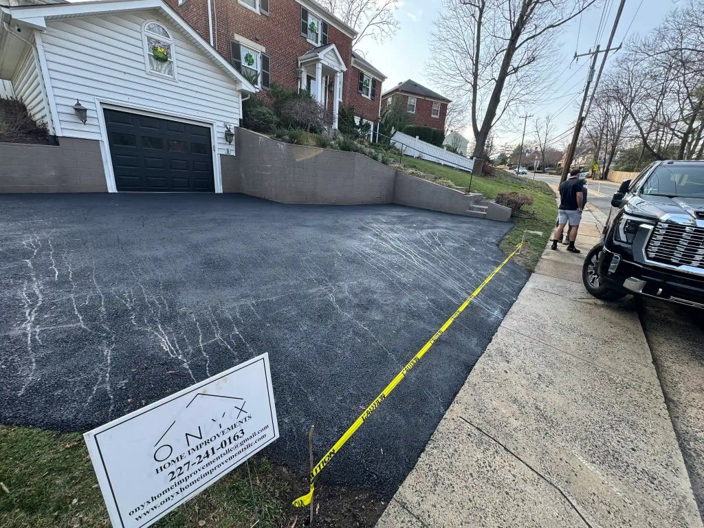 Freshly poured asphalt driveway with yellow safety ribbon barrier.