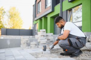 A masonry contractor installs pavers using a rubber mallet in a backyard.