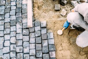 A paving company worker installs pavers on sand, using a rubber mallet.