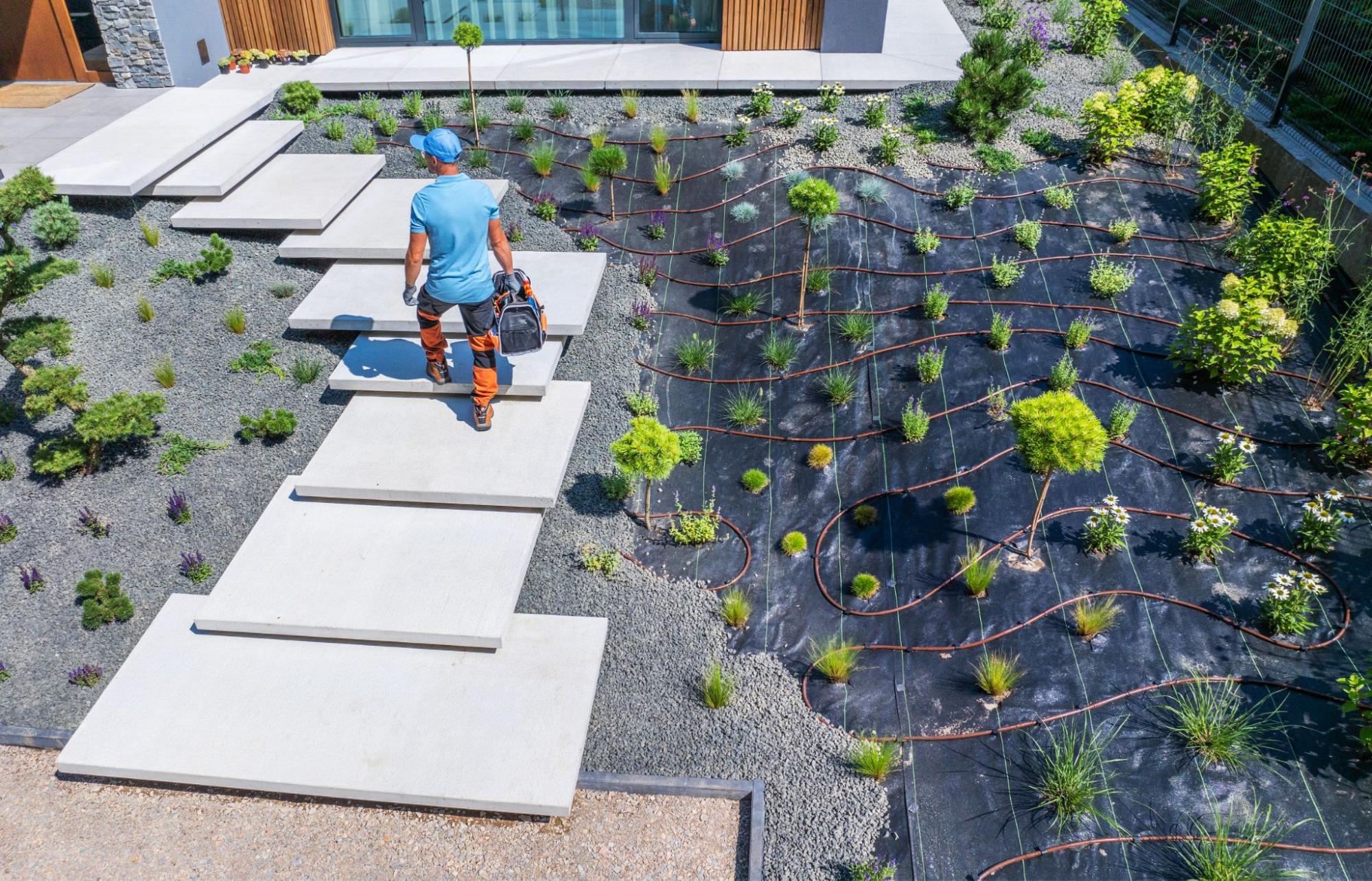 A worker steps across a modern walkway in a freshly landscaped backyard.