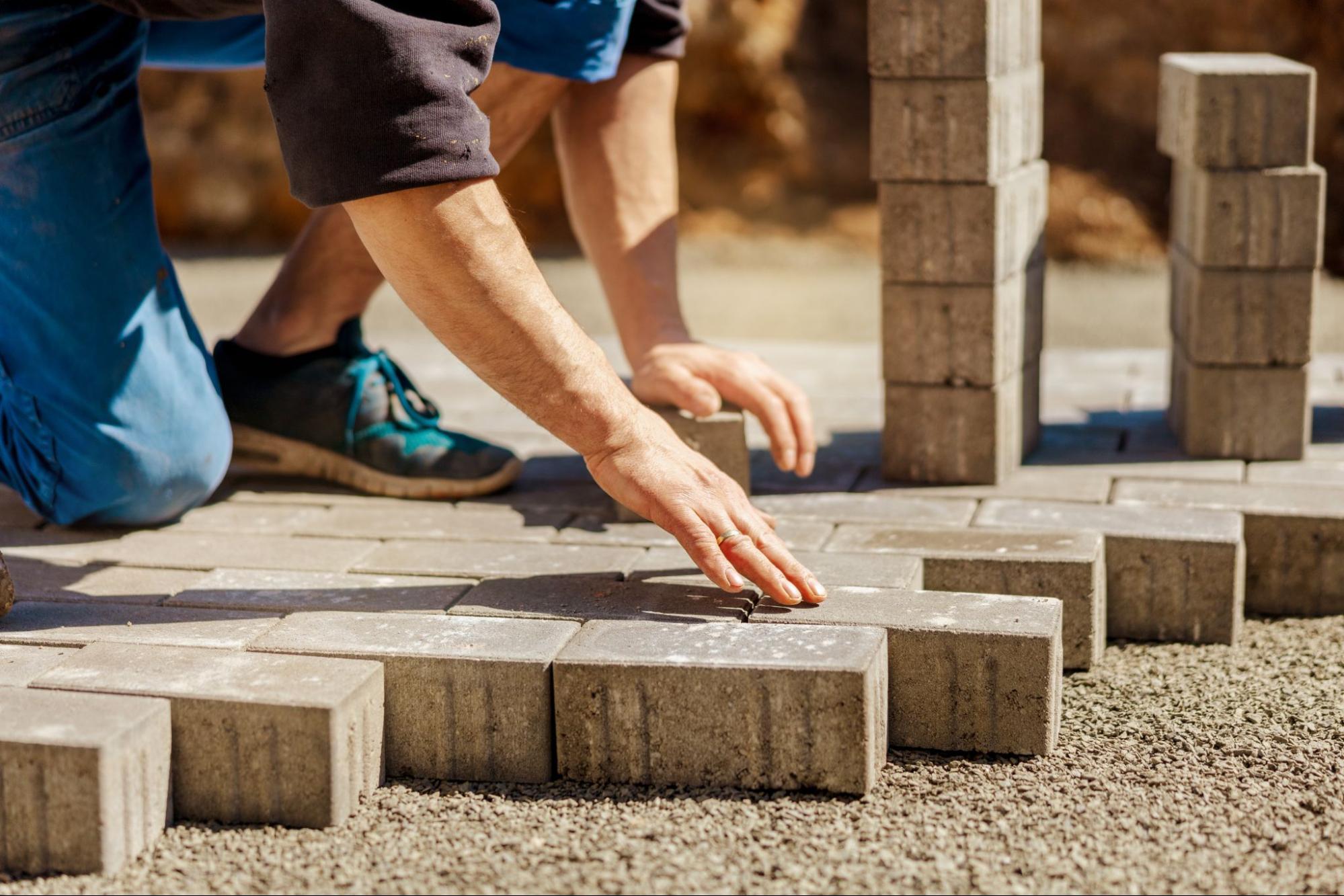 A paving company worker installs individual pavers by hand.