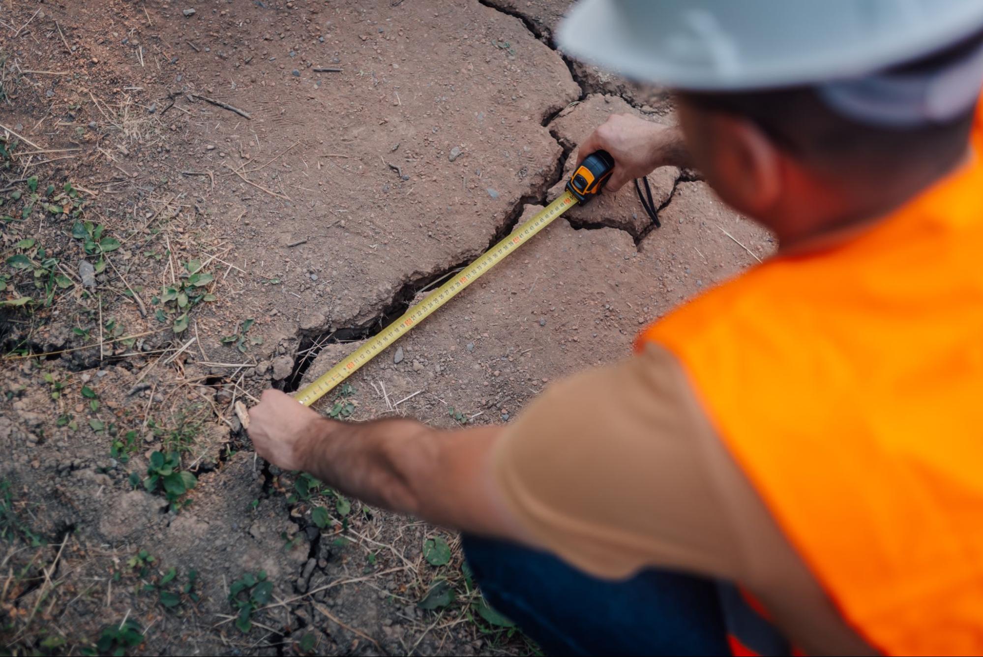A construction worker measures a crack in a concrete foundation.