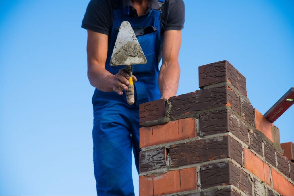 A bricklayer repairing and setting masonry on a rooftop chimney