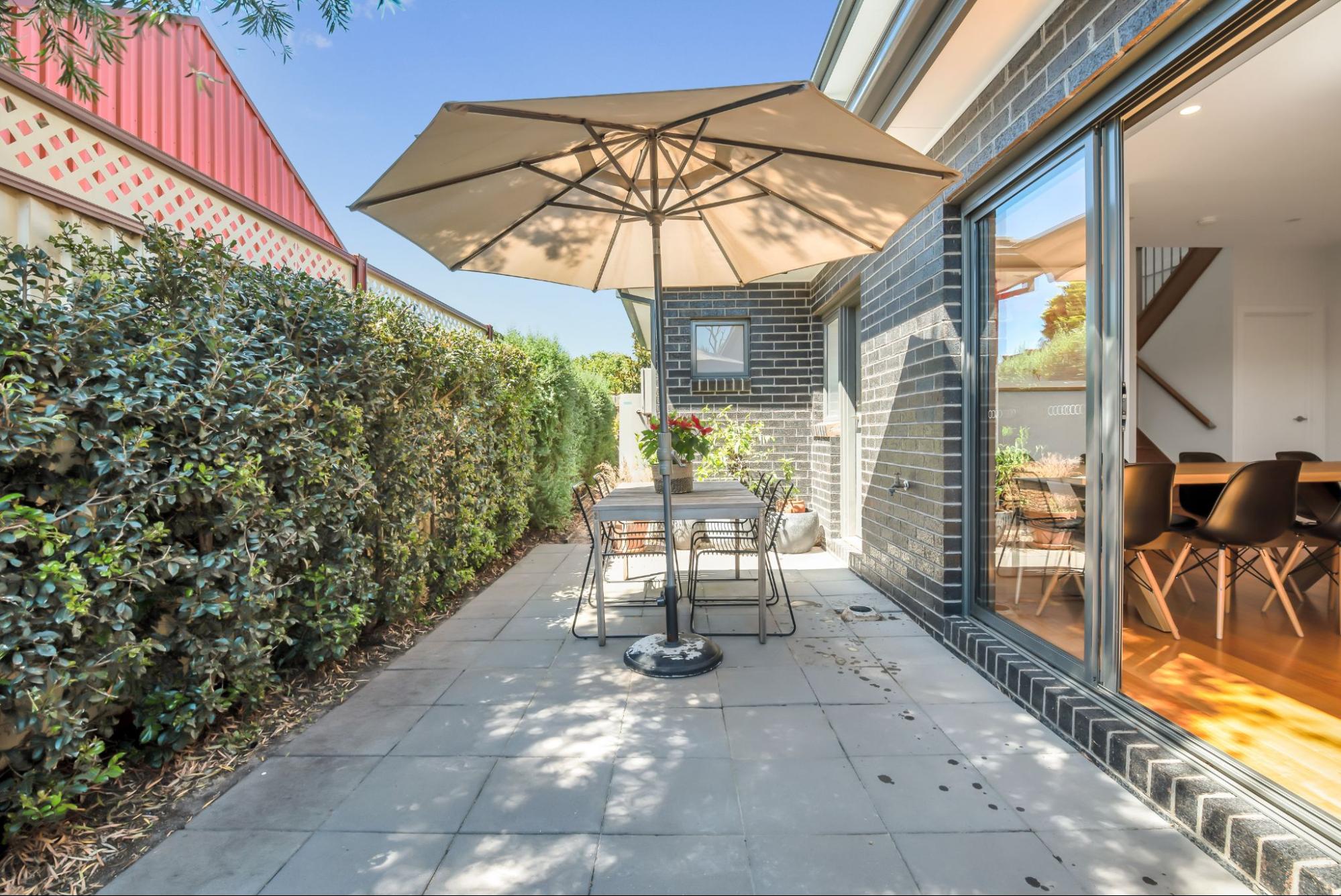 A bluestone patio with a pergola and dining set outside a new house