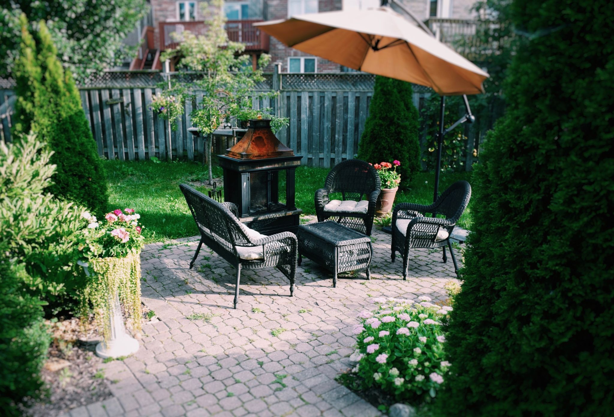Patio furniture on a stone patio next to flowers and shrubbery.