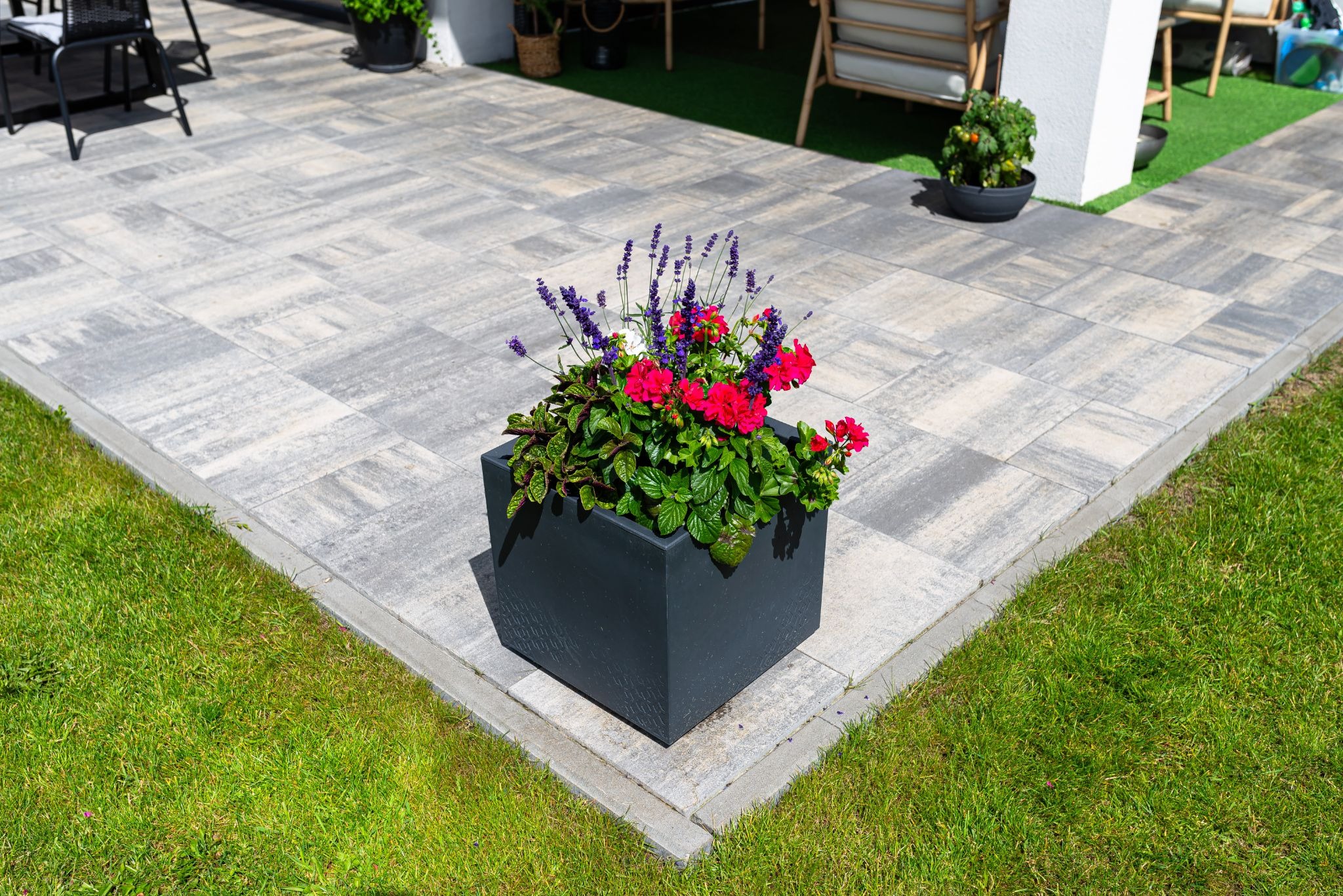 Potted flowers on a modern stone patio next to grass.
