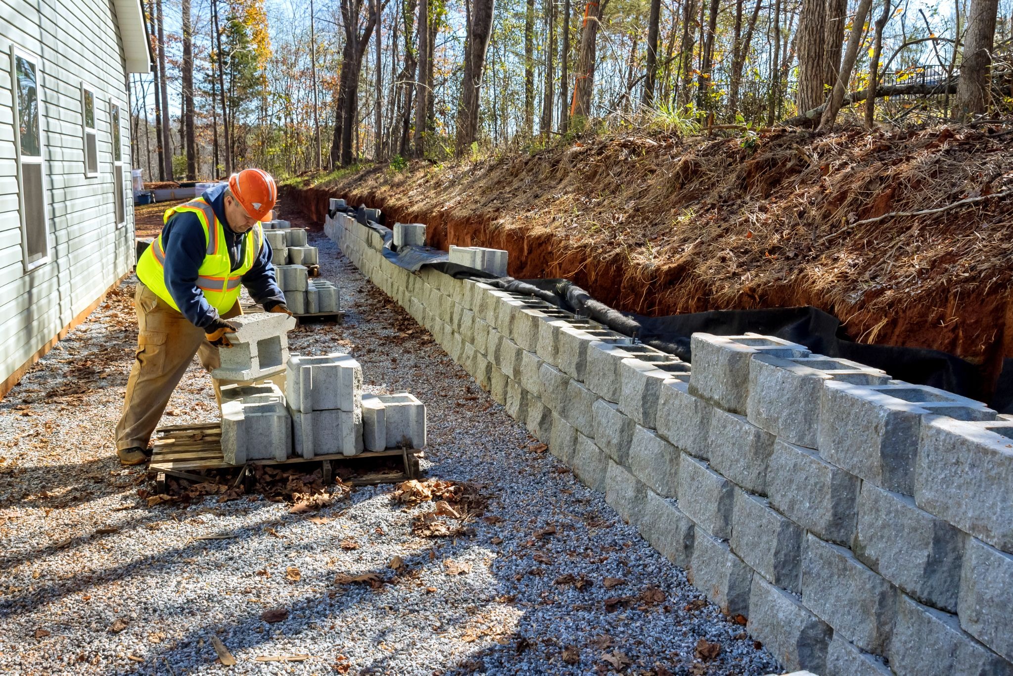 Worker in a hard hat installing a stone retaining wall.