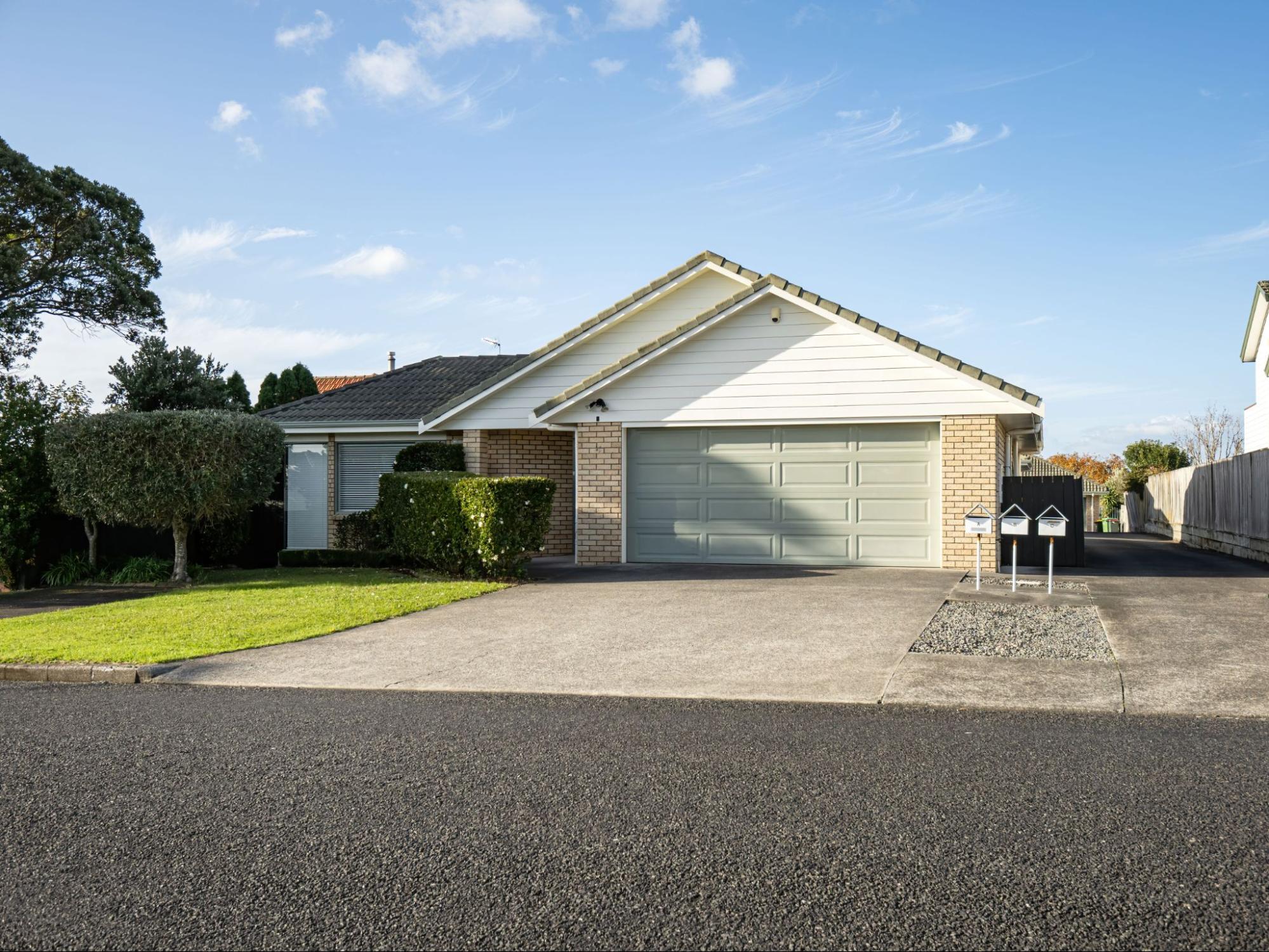 Suburban garage with a roller door, smooth concrete driveway, and adjoining asphalt road in a quiet residential street