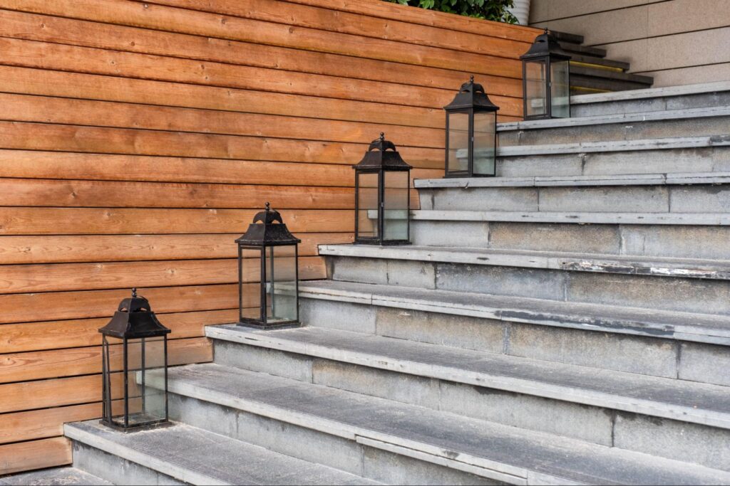 Stone stairs next to lanterns and a wooden wall.