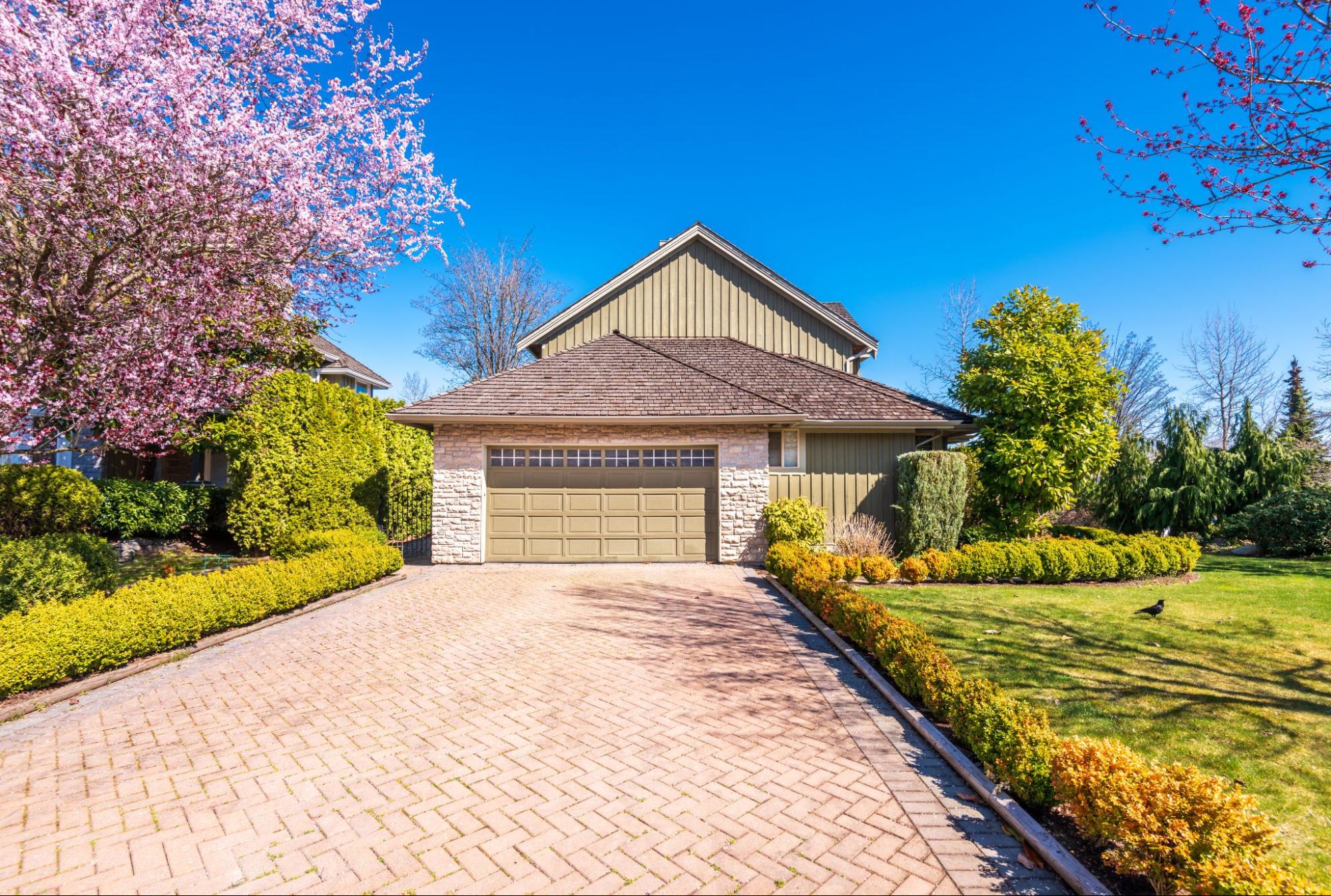 Paver driveway with elegant stone pattern, bordered by landscaped garden, leading to a luxury home garage