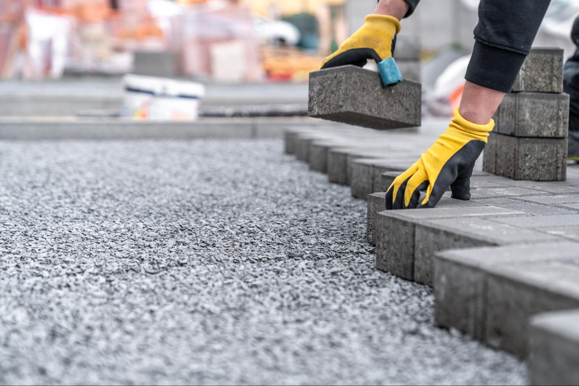Construction worker installing interlocking pavers on a residential driveway with compacted base and tools visible