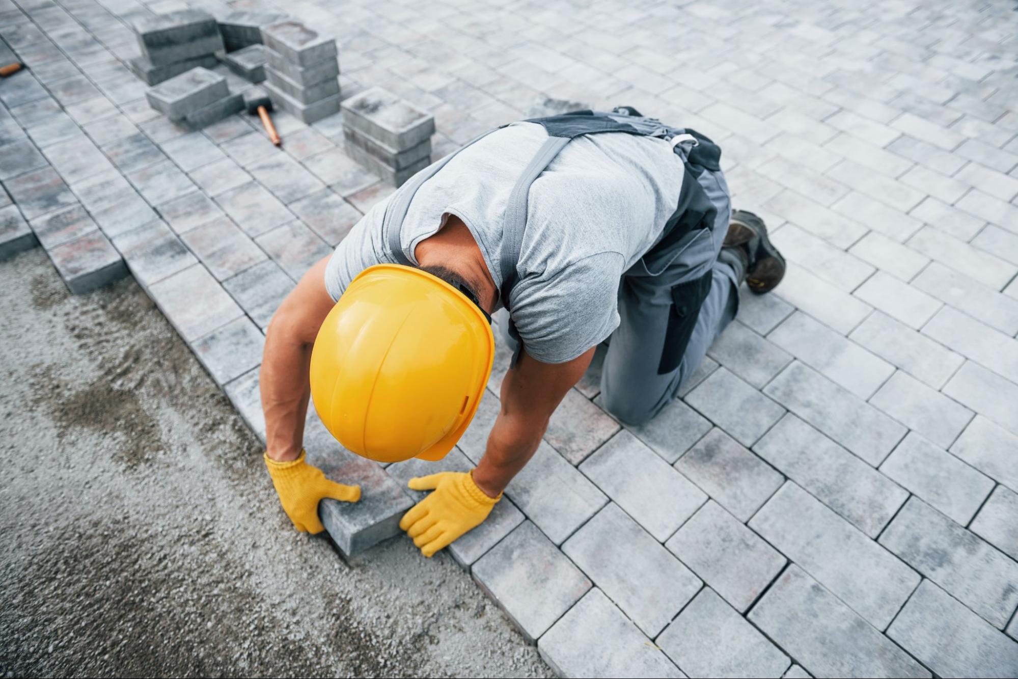 Paving contractor in a hard hat laying paving stones.