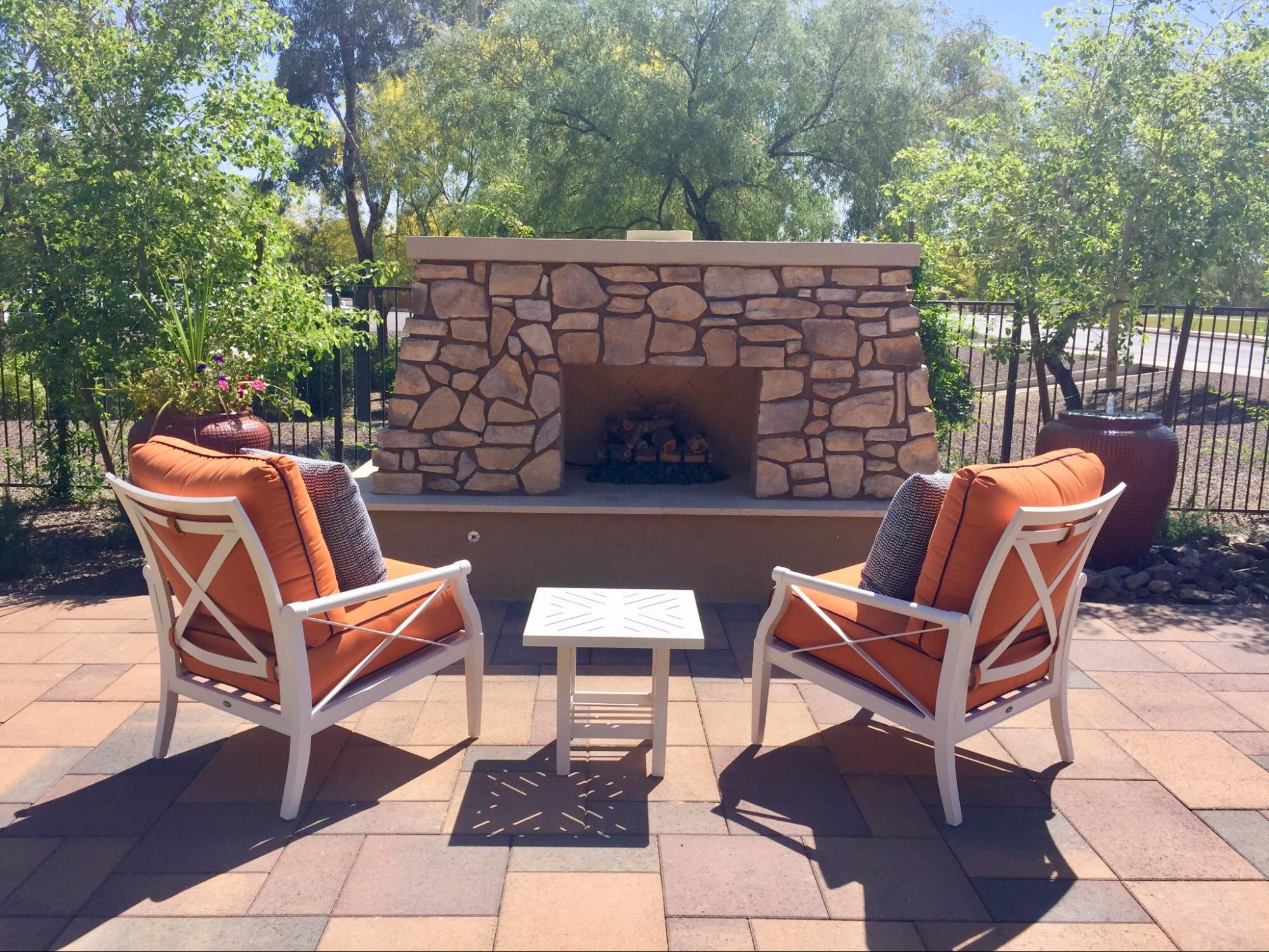 Two cushioned lounge chairs facing an outdoor fireplace in a cozy patio setting